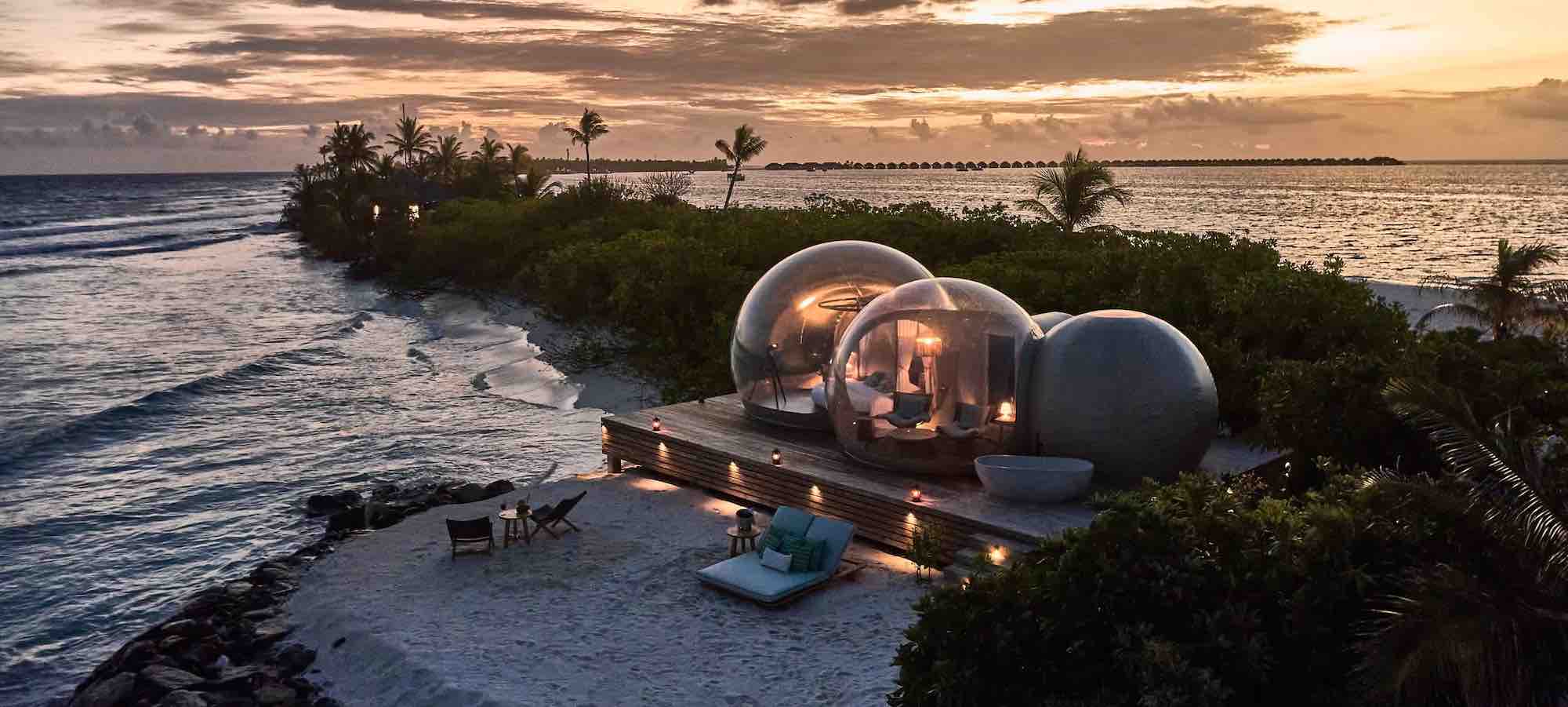 A bubble hotel on a wooden platform, next to a small wooden beach surrounded by vegetation and with a couple of loungers to contemplate the sea