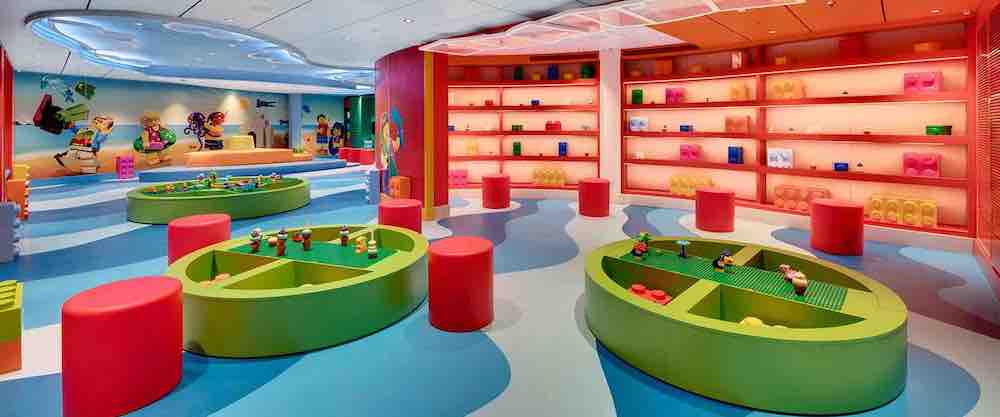 A child care room full of green toys and tables where children can play and where they can sit on a red seat