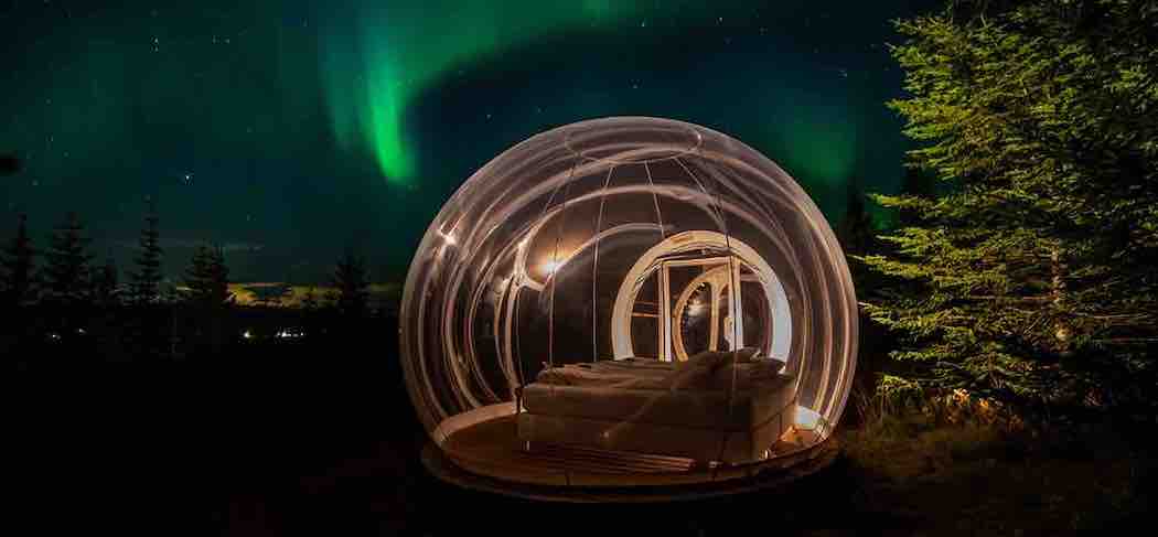 
A bubble hotel located in a forest with the green northern lights in the background