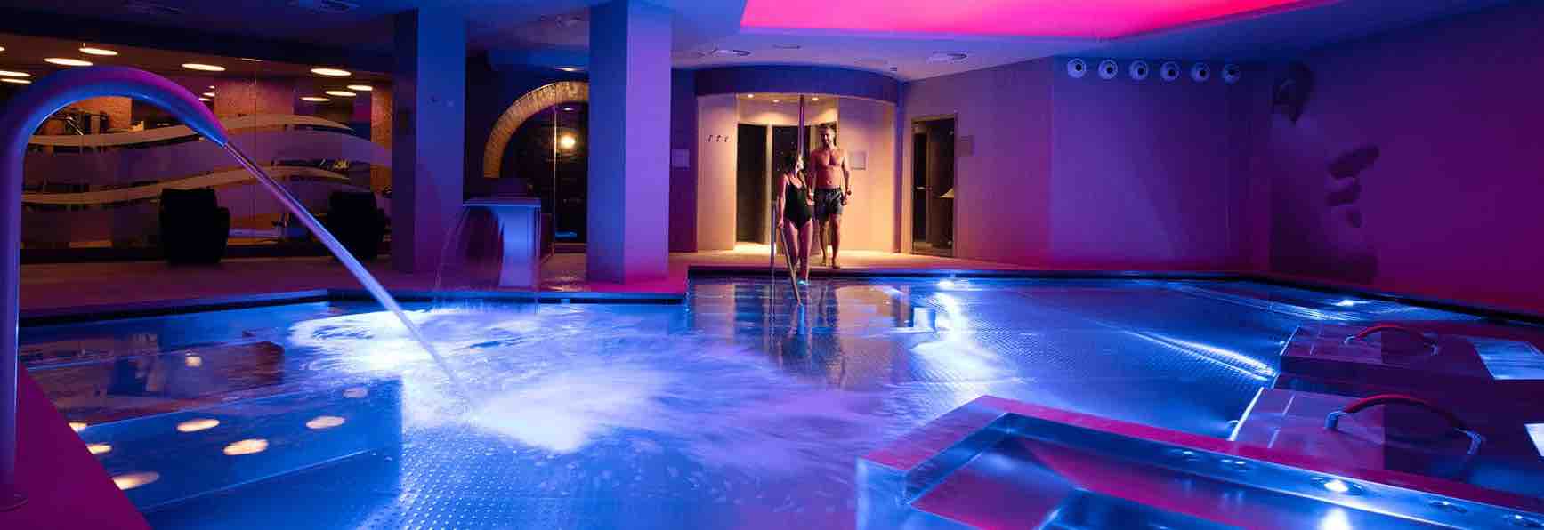 A wellness center room with chromotherapy lights and a couple going down the stairs to the heated pool
